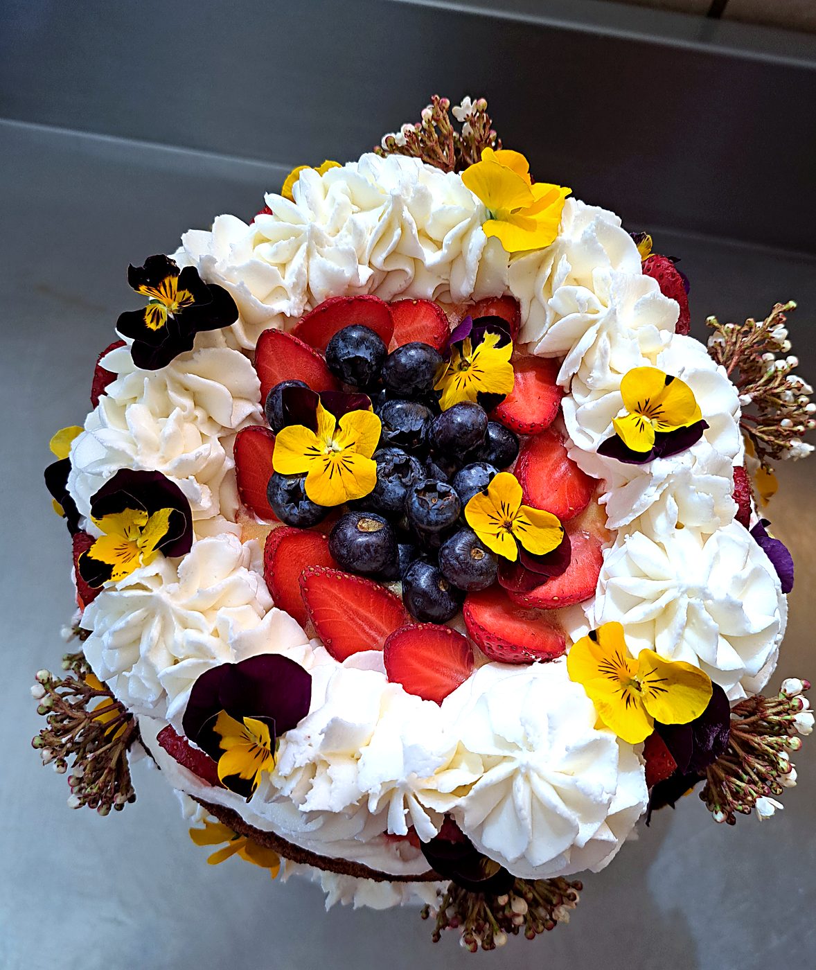 Wedding cake from above: cream rosettes, berries and edible pansies